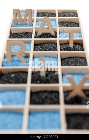 Low angle view of a wooden box with square compartments rectangular compartments filled with blue or black decorative sand and the letters M, A, T, R, Stock Photo