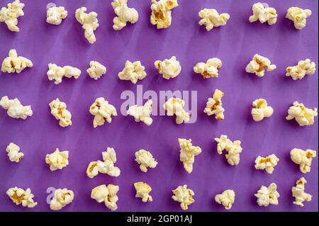 Popcorn pattern isolated on purple background, top view. Pop corn texture, tasty wallpaper design, movie or cinema food concept Stock Photo