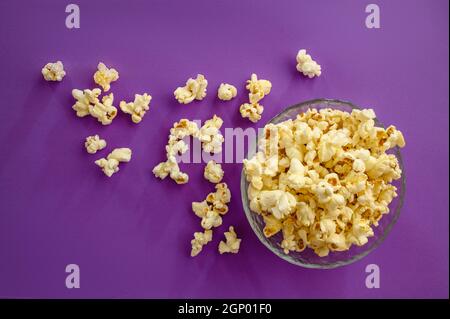 Popcorn in plate isolated on purple background, top view. Pop corn texture, tasty wallpaper design, movie or cinema food concept Stock Photo