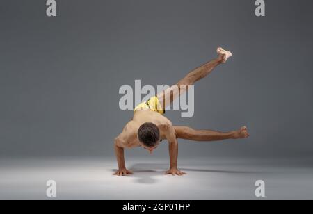 Muscular yoga stands on hands in difficult pose, meditation position, grey background. Strong man doing yogi exercise, asana training, top concentrati Stock Photo