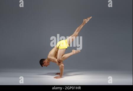 Muscular yoga stands on hands in difficult pose, meditation position, grey background. Strong man doing yogi exercise, asana training, top concentrati Stock Photo