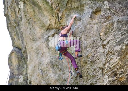 Determined girl climber clambering up steep wall of rocky mountain. Sportswoman overcoming difficult route. Engaging in extreme sports and rock climbi Stock Photo
