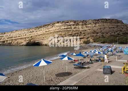 Matala, Crete - October 17 2010: Beautiful beach with tourists enjoying the sunSandstone rugged cliffs with caves which are Roman graves  Landscape as Stock Photo