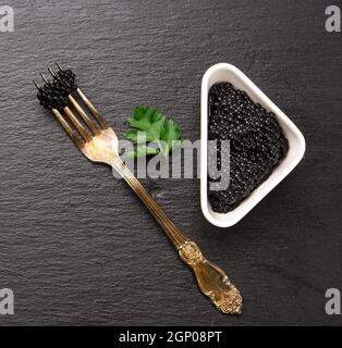 black grainy caviar of paddlefish fish in a white ceramic bowl, black background, top view Stock Photo