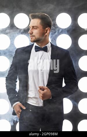 handsome man in tuxedo posing against the backdrop of spotlights and smoke. night life Stock Photo