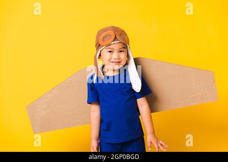 Happy Asian handsome funny child or kid little boy smile wear pilot hat playing and goggles with toy cardboard airplane wings flying, studio shot isol Stock Photo