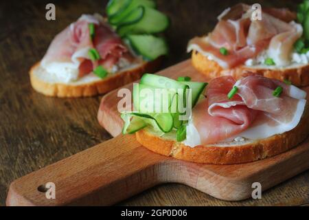 Traditional italian appetizer bruschetta of toasted bread with ricotta cheese, cucumber and prosciutto . Stock Photo