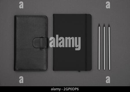Close up two closed black leather cover notebooks and pencils over grey paper background, flat lay, directly above Stock Photo