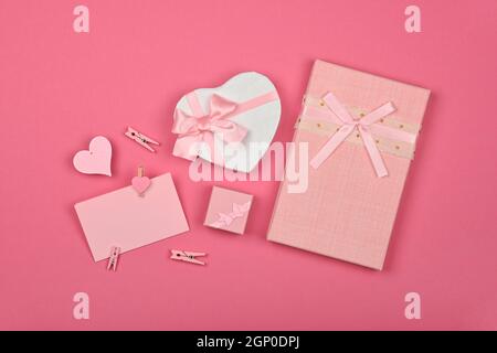 Valentine template of heart shaped gift boxes with ribbon chiffon bow and paper note over pink wrapping paper background, close up flat lay, elevated Stock Photo