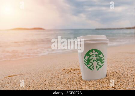 THASSOS, GREECE - AUGUST 21 2018 Starbucks paper cup of coffee on the sea water and beach sandy background Stock Photo