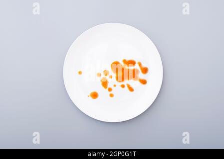 White ceramic plate with leftover food, drops, blots of sauce on a dish surface. Top view, on grey surface Stock Photo