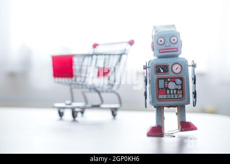 Online-Shopping concept: Toy robot and Miniature shopping cart Stock Photo