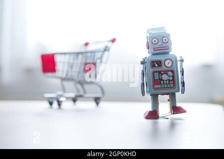 Online-Shopping concept: Toy robot and Miniature shopping cart Stock Photo