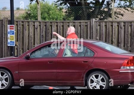 An angry man queuing for fuel at a petrol station in the UK loses his patience, exits his car and shouts angrily at a car already filling up Stock Photo