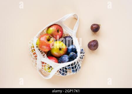 Fresh apples, plums and figs in a string bag on light beige peachy background. Zero waste, no plastic concept. Top view, flat lay. Stock Photo