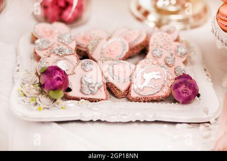 Delicious desserts at the wedding candy bar in the buffet area: cookies covered with icing, decorated with angels, cameo, sugar rosebuds and silver dy Stock Photo