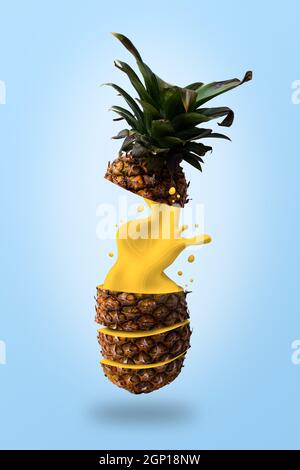 Ripe pineapple flying with yellow juice exploding on light blue background. Fruit design for packaging. Stock Photo