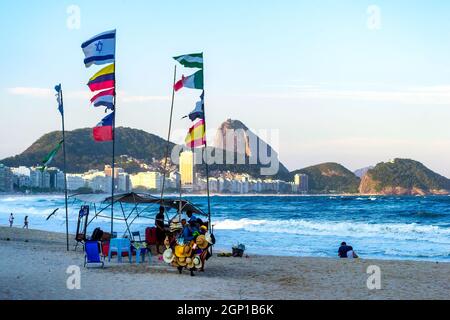 Souvenir kiosk with diverse national flags in the sand of the Copacabana beach in Rio de Janeiro, Brazil. This place is a famous tourist attraction in Stock Photo