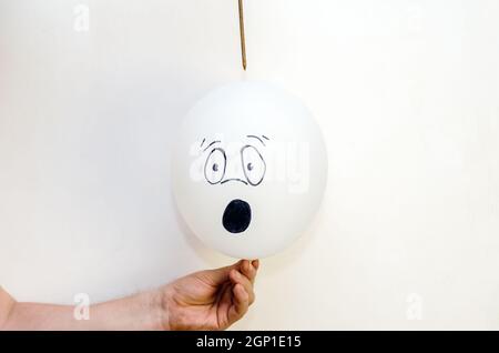 A balloon with a face painted on it and a rusty nail. Man holdin Stock Photo