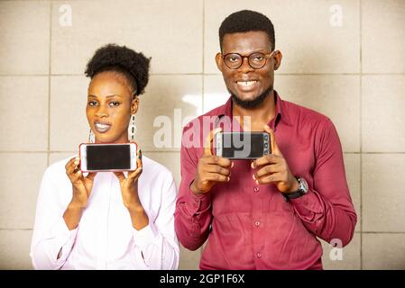 Two students stand together and hold their phones in their hands. Looking at the camera and smiling. Young beautiful happy people. very well dressed a Stock Photo