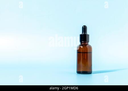 Glass dropper bottle made of brown glass on a blue background casts a shadow. Front view with copy space. Mockup of a cosmetic product. Serum for skin Stock Photo