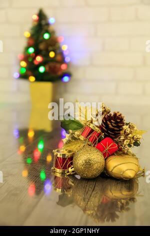Christmas decoration with reflection on a dark worktop and  blurred Christmas tree with lights in the background Stock Photo