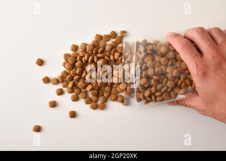 Man's hand dropping dog kibble from a clear plastic bag onto a white table. Top view. Horizontal composition. Stock Photo