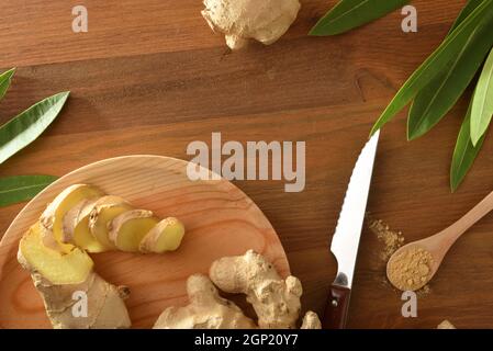Ginger root slice on  and spoon with powder on wooden table with root and leaves. Top view. Stock Photo