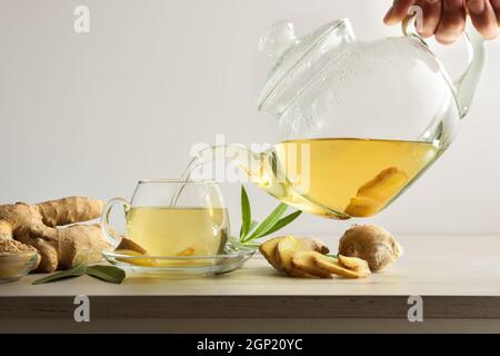 Man serving cup with ginger root infusion on kitchen bench with root and slices white isolated background. Front view. Stock Photo