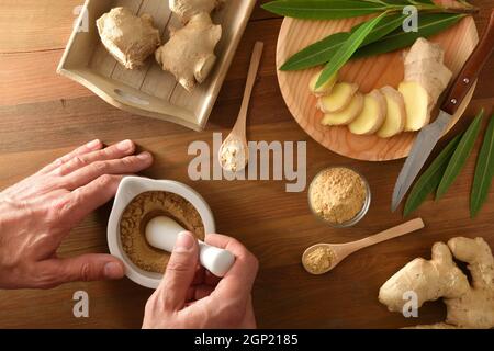 Hands preparing  ginger powder for curative and culinary purposes with ginger root sliced in portions on wooden table. Top view. Stock Photo