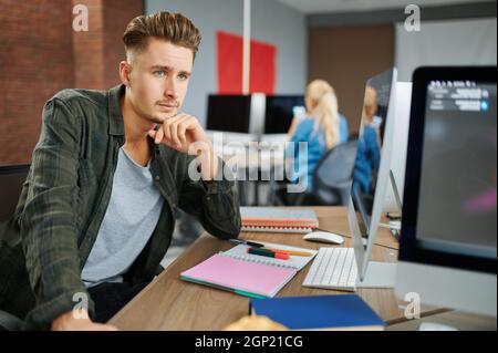 Thoughtful male IT specialist sits at the table in office. Web programmer or designer at workplace, creative occupation. Modern information technology Stock Photo