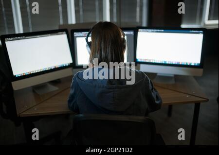 Female internet hacker in headphones works on computer in dark office. Illegal web programmer at workplace, criminal occupation. Data hacking, cyber s Stock Photo