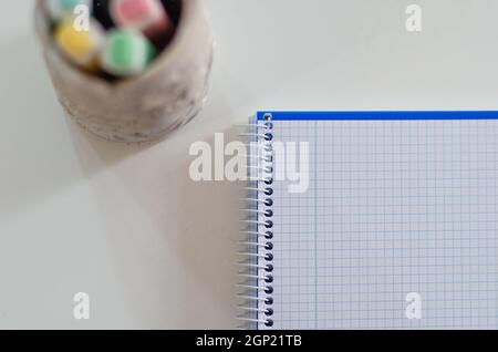 Several colored pencils in a ceramic piece are placed on a wooden table and a white notebook. Back to school concept Stock Photo