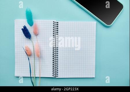 Opened notepad and phone on blue background. Office stationery supplies, school or education accessories, writing and drawing tools Stock Photo