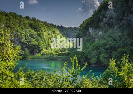 Tall cliff, valley, turquoise coloured lake and tourists enjoying walks on boardwalks in Plitvice Lakes, National Park UNESCO World Heritage, Croatia Stock Photo