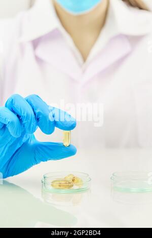 Close up Scientist hands putting in nitrile blue latex gloves holding Omega 3 capsule in labcoat wearing nitrile gloves, doing experiments in lab Stock Photo