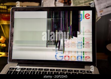 Laptop with a smashed screen (MacBook Pro, Retina 13-inch 2015) with a glitchy screen caused by breakage damage, a crack chip in the monitor screen. Stock Photo