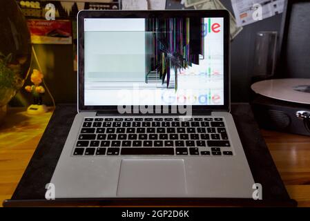 Laptop with a smashed screen (MacBook Pro, Retina 13-inch 2015) with a glitchy screen caused by breakage damage, a crack chip in the monitor screen. Stock Photo