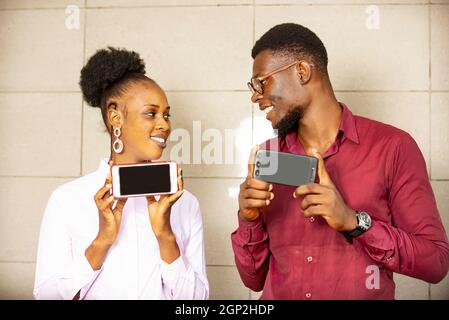 Two students stand together and hold their phones in their hands. Looking at the camera and smiling. Young beautiful happy people. very well dressed a Stock Photo