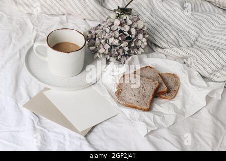 Feminine still life scene.Summer breakfast in bed composition. Cup of coffee, dry hydrangea flowers and nuts bread on crinckled paper. Blank greeting Stock Photo