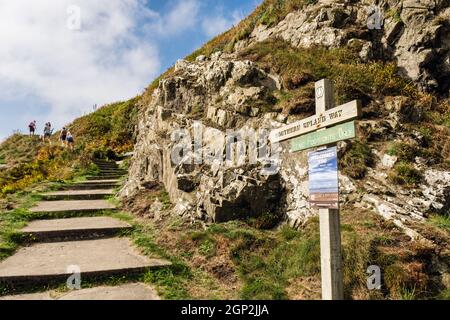 Signpost and steps at western start of Southern Upland Way with people walking. Portpatrick, Dumfries and Galloway, Scotland, UK, Britain Stock Photo