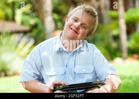 Close up portrait of handicapped boy playing on digital tablet outdoors. Stock Photo