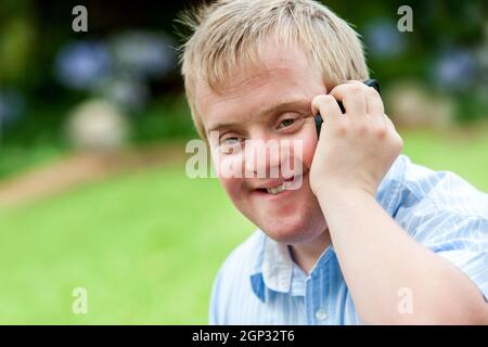 Close up portrait of handicapped boy talking on smart phone outdoors. Stock Photo