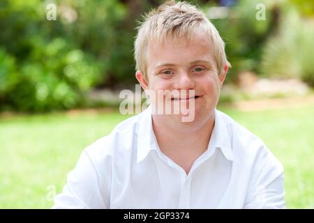 Close up portrait of boy with down syndrome in white shirt outdoors. Stock Photo