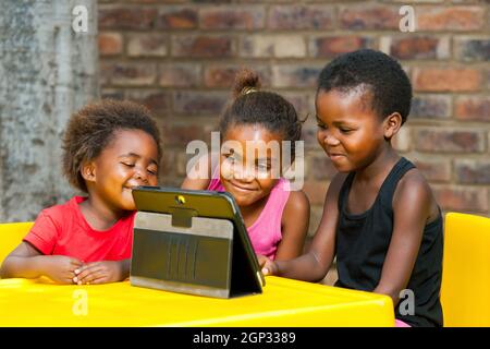 Three african kids playing together on tablet.