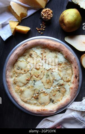 Pizza with dried pears and pine nuts. Traditional Italian pizza. Metal plate for serving pizza. A piece of parmesan and a pear on a dark background. W Stock Photo