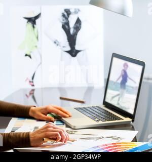 Extreme close up of Fashion Designers hands creating new collection on paper and laptop. Stock Photo