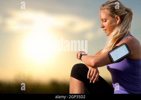 Portrait of young athlete checking workout on smart watch at sunset.Woman wearing armband with smart watch and graphic showing workout results. Stock Photo