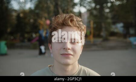 Young handsome blond hair colored eyed boy standing in the park, looking at camera and smiling Stock Photo