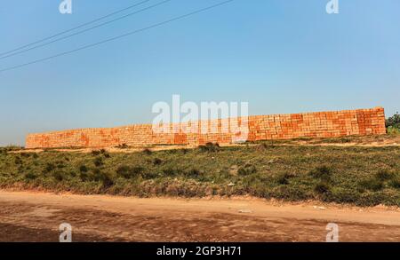 Orange red bricks made from local clay arranged in wide stack, ready for building a house near the road. Stock Photo